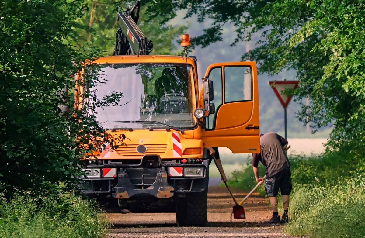 Ein orangenes Baufahrzeug steht auf einer Straße. Ein Mann kehrt die Straße.